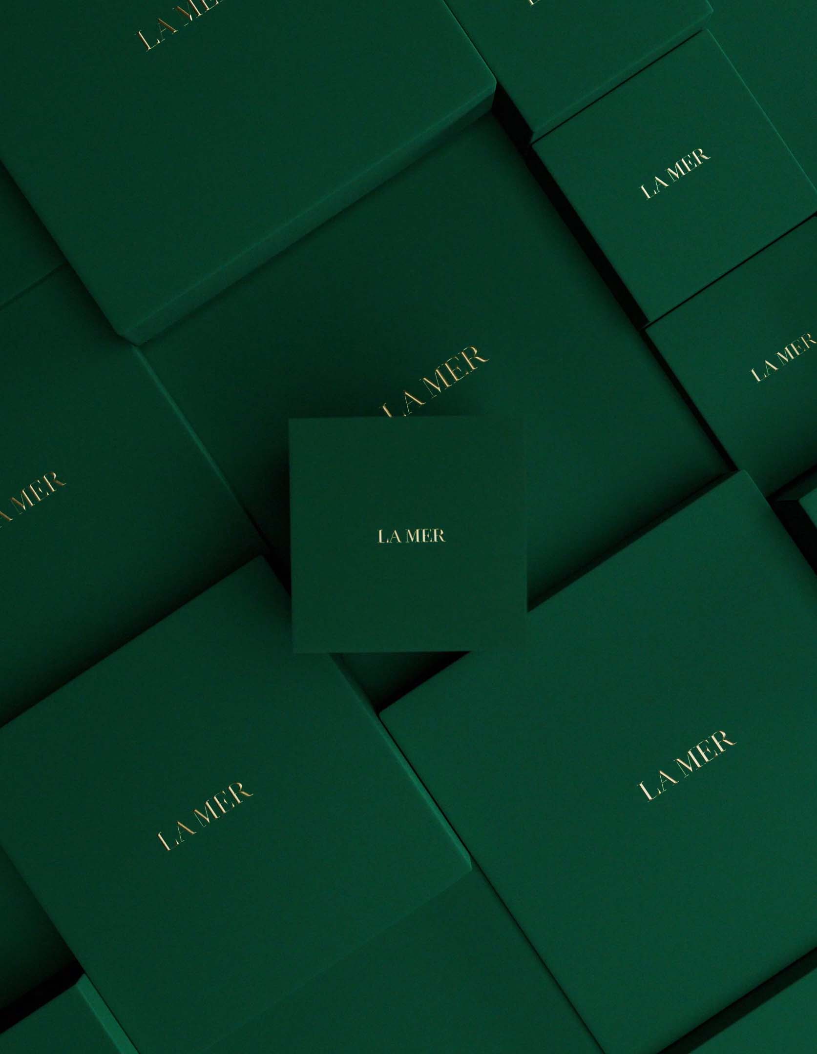 Image of multiple green la mer gift boxes laid out on an angle and one la mer box straight on in view.